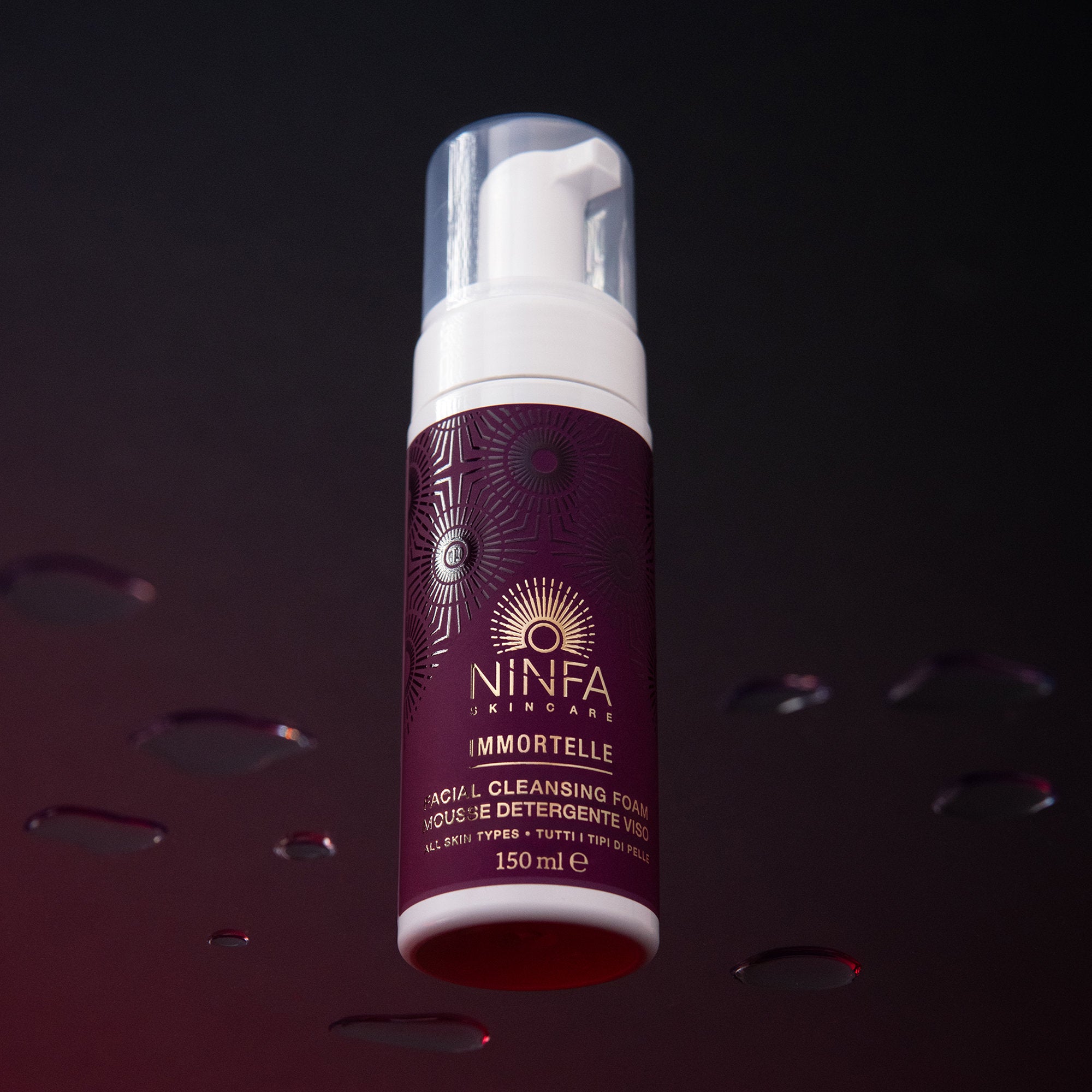 Mousse detergente all’elicriso di Ninfa Skincare su vetro con gocce e sfondo viola scuro
