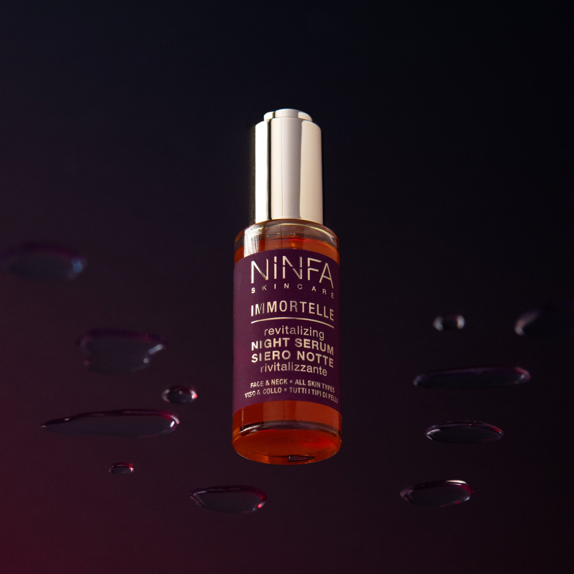Primo piano del siero rivitalizzante all’elicriso di Ninfa Skincare su vetro con gocce intorno e sfondo viola scuro