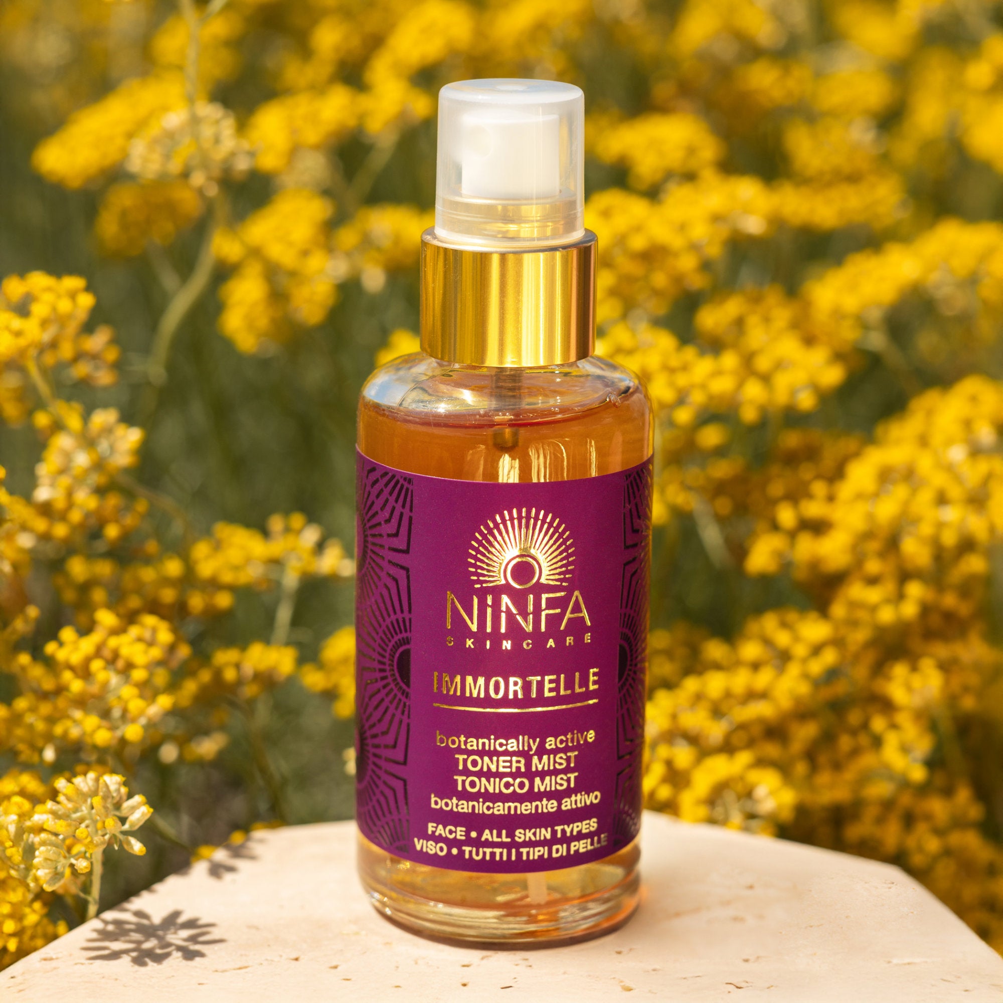 Primo piano del tonico viso all’elicriso di Ninfa Skincare con sfondo di campo di elicriso italico in fiore