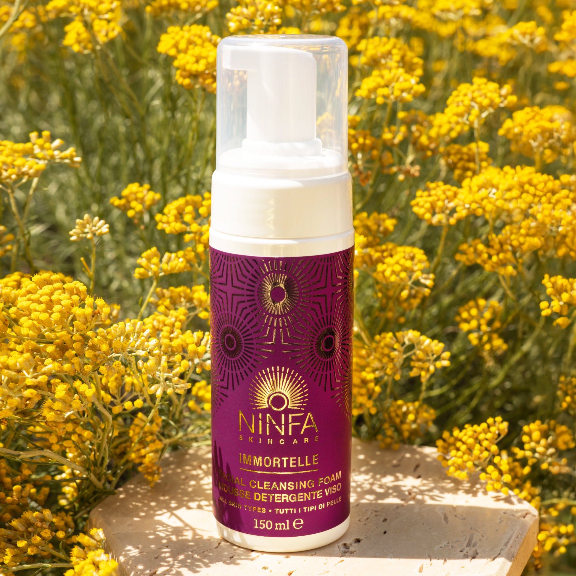 Primo piano della mousse detergente all’elicriso di Ninfa Skincare con sfondo di campo di elicriso italico in fiore