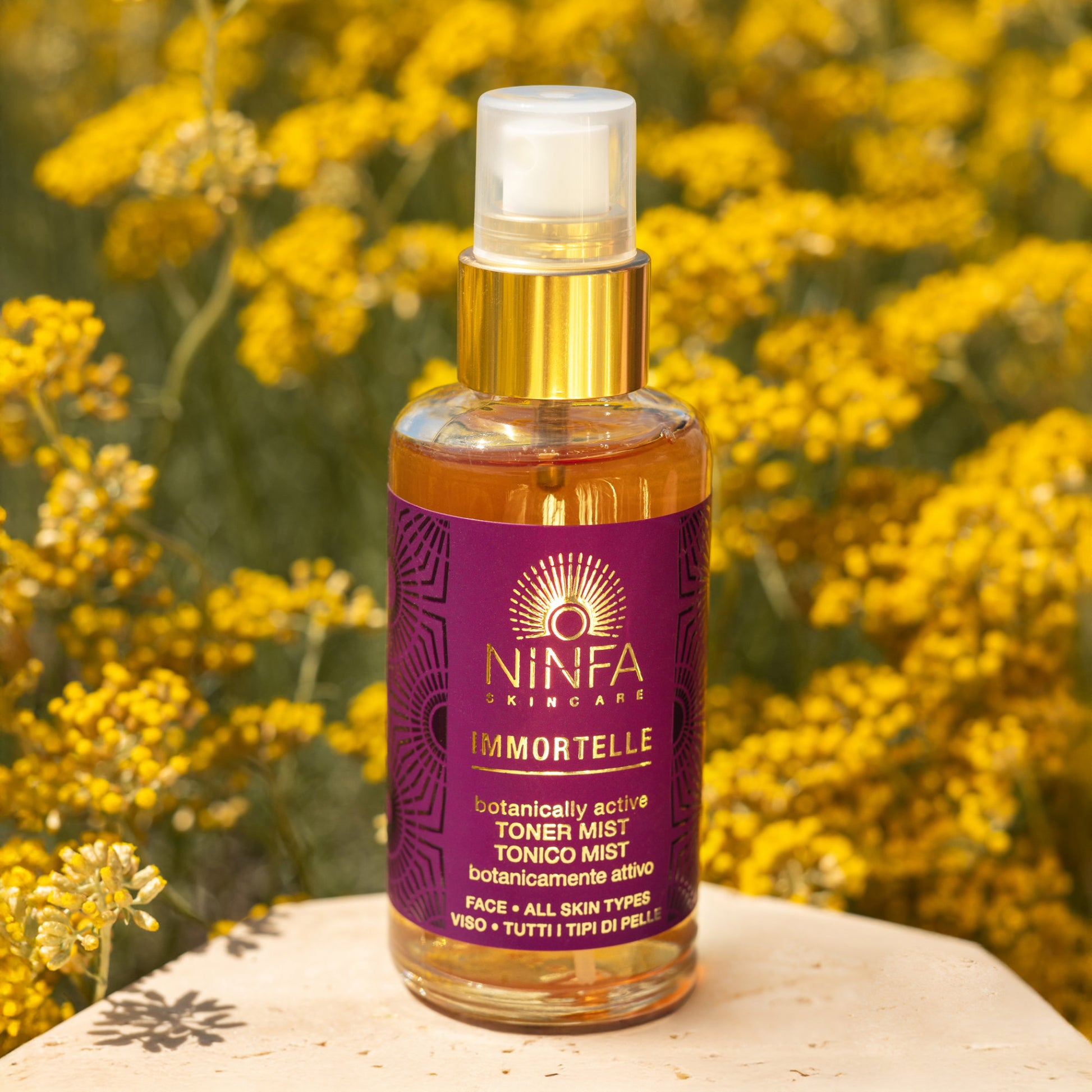 Primo piano del tonico viso all’elicriso di Ninfa Skincare con sfondo di campo di elicriso italico in fiore