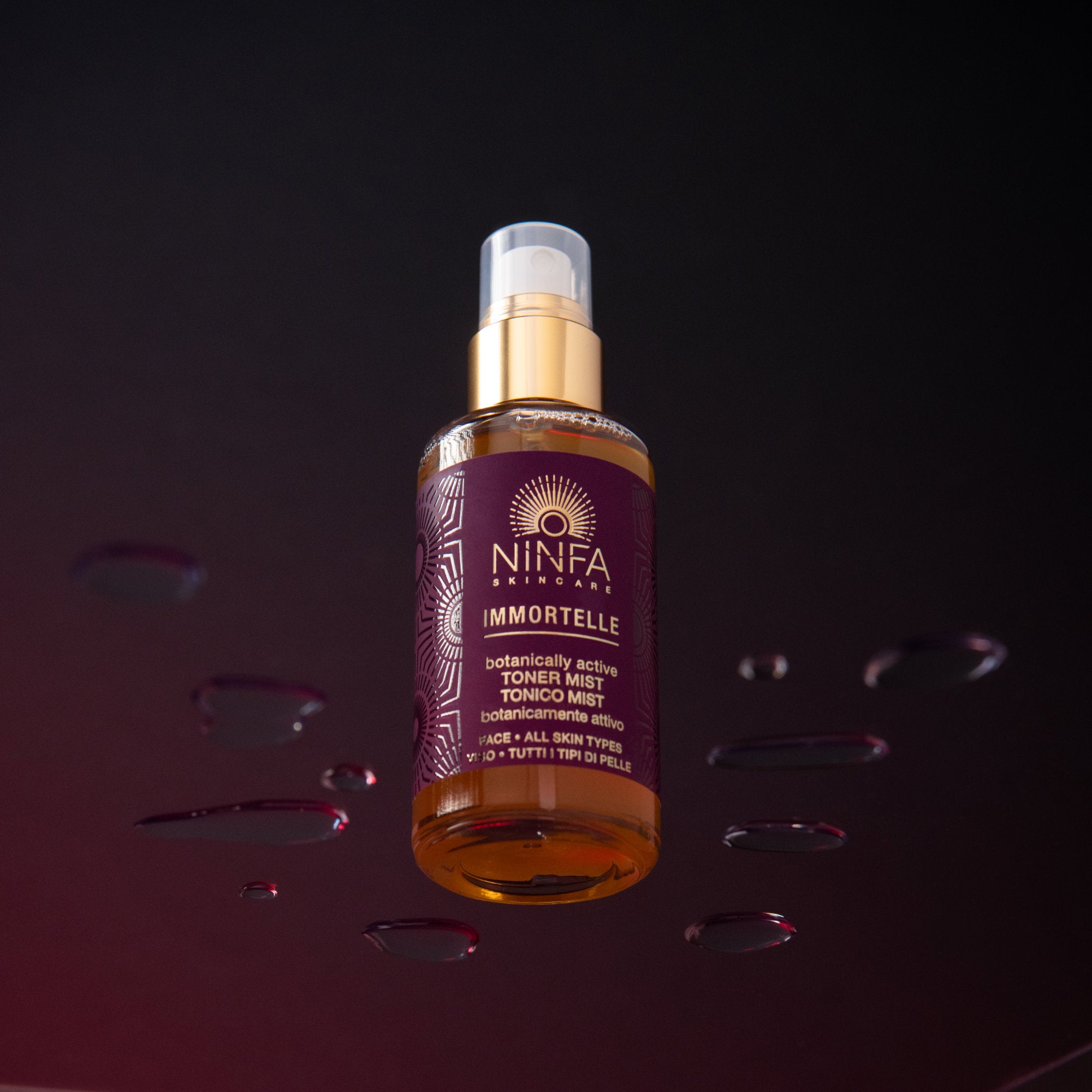 Tonico viso all’elicriso di Ninfa Skincare su vetro con gocce e sfondo viola scuro